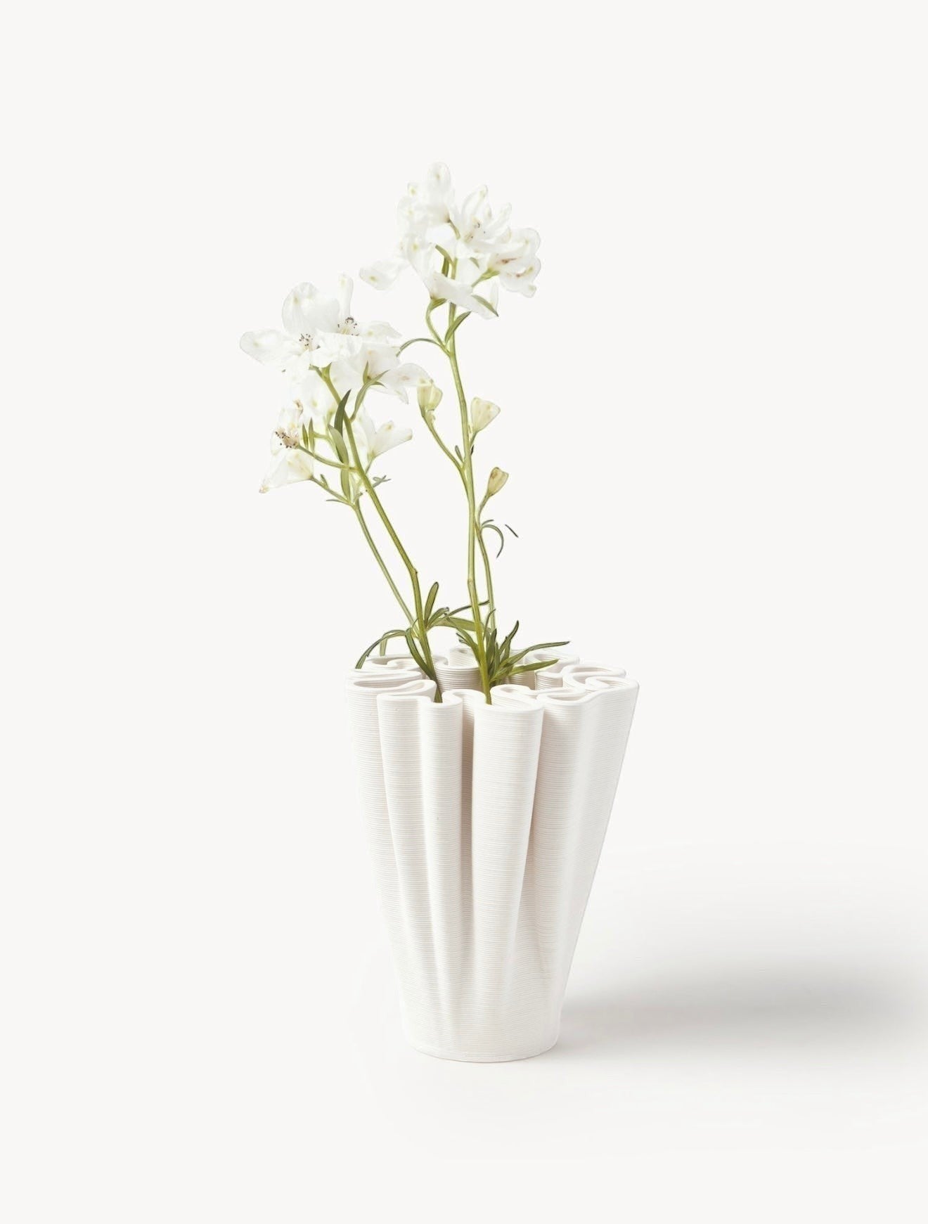 VALMORA off-white ceramic sculptural vase with fluted design holding white flowers.